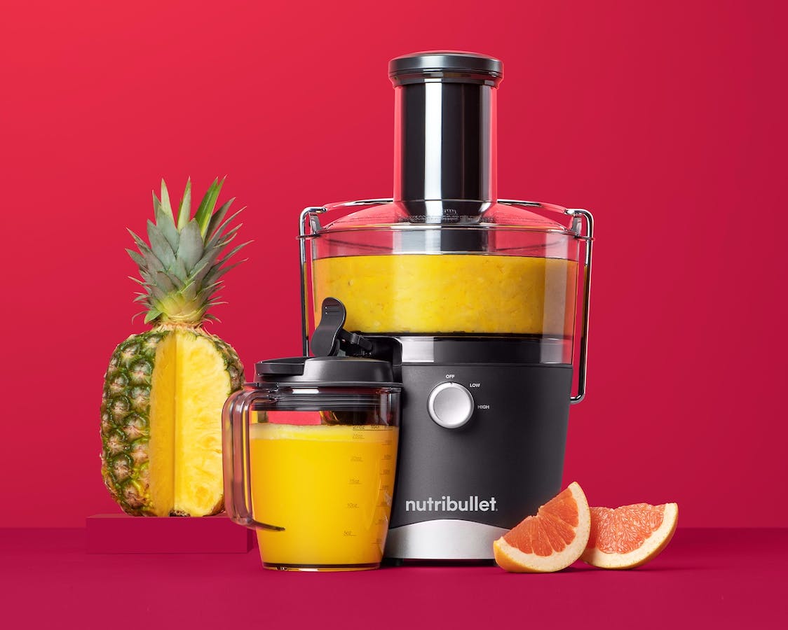 nutribullet Juicer with pineapple and grapefruit on red background.