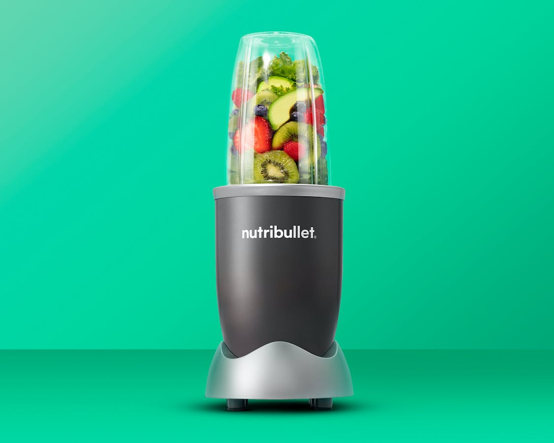 nutribullet original with fruit and vegetables on green background.